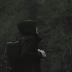 Side view of a man in a hoodie with a backpack, isolated in a dark natural setting.